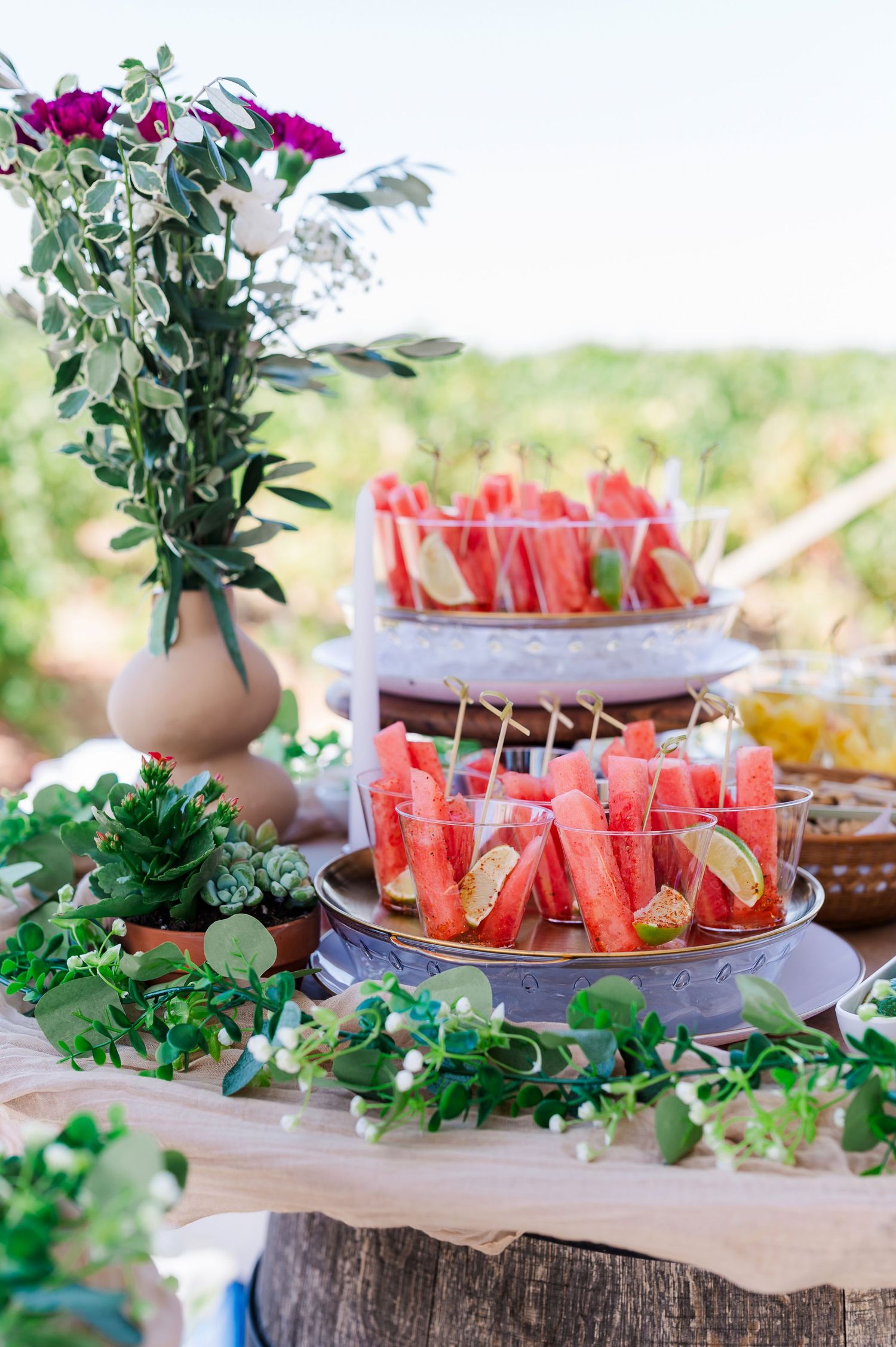 Fresh watermelon cubes arranged on rustic wooden serving platters with greenery and floral decorations at an outdoor party.