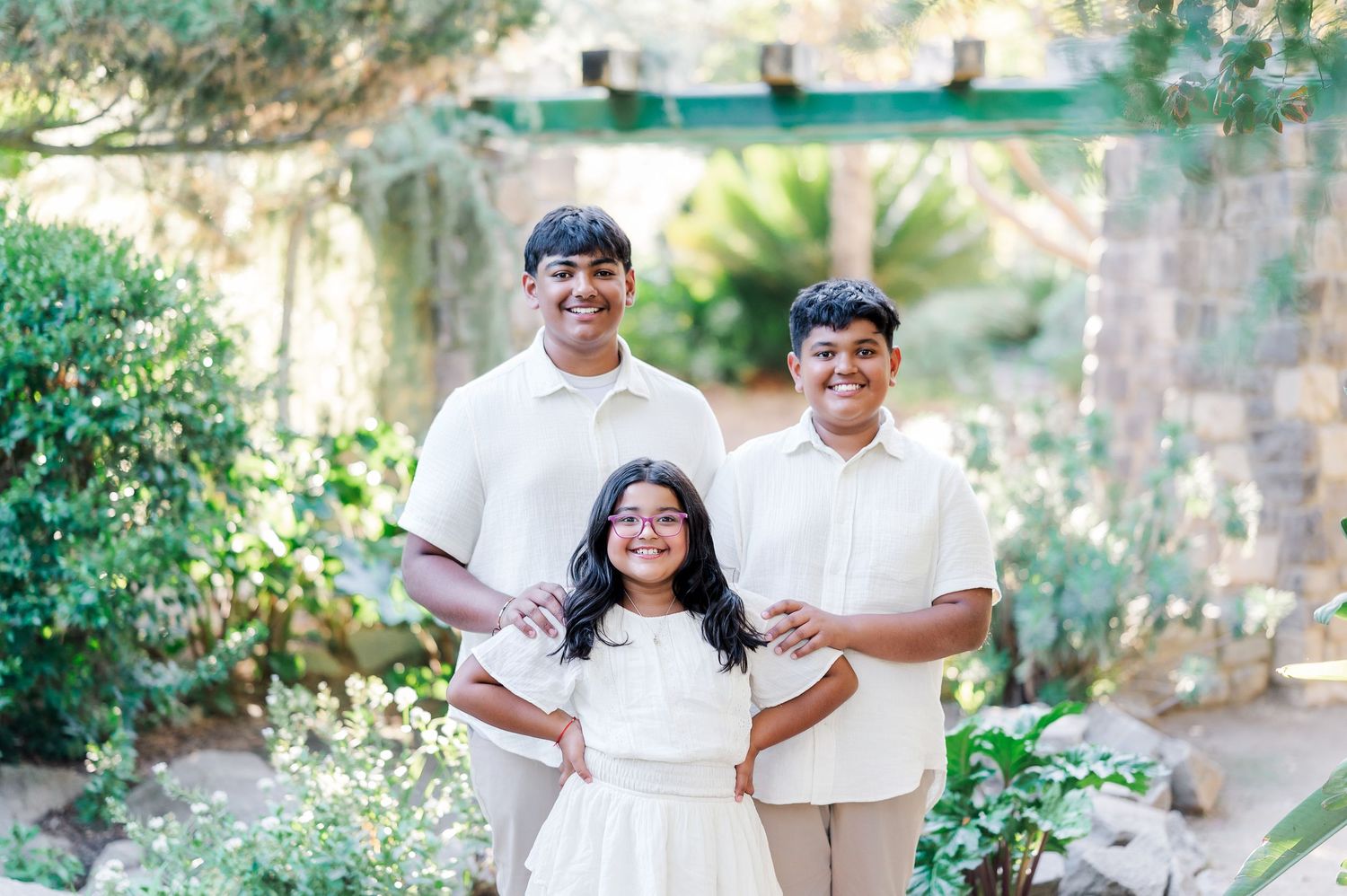 Family members pose together in a garden setting wearing coordinated white outfits for outdoor portraits.