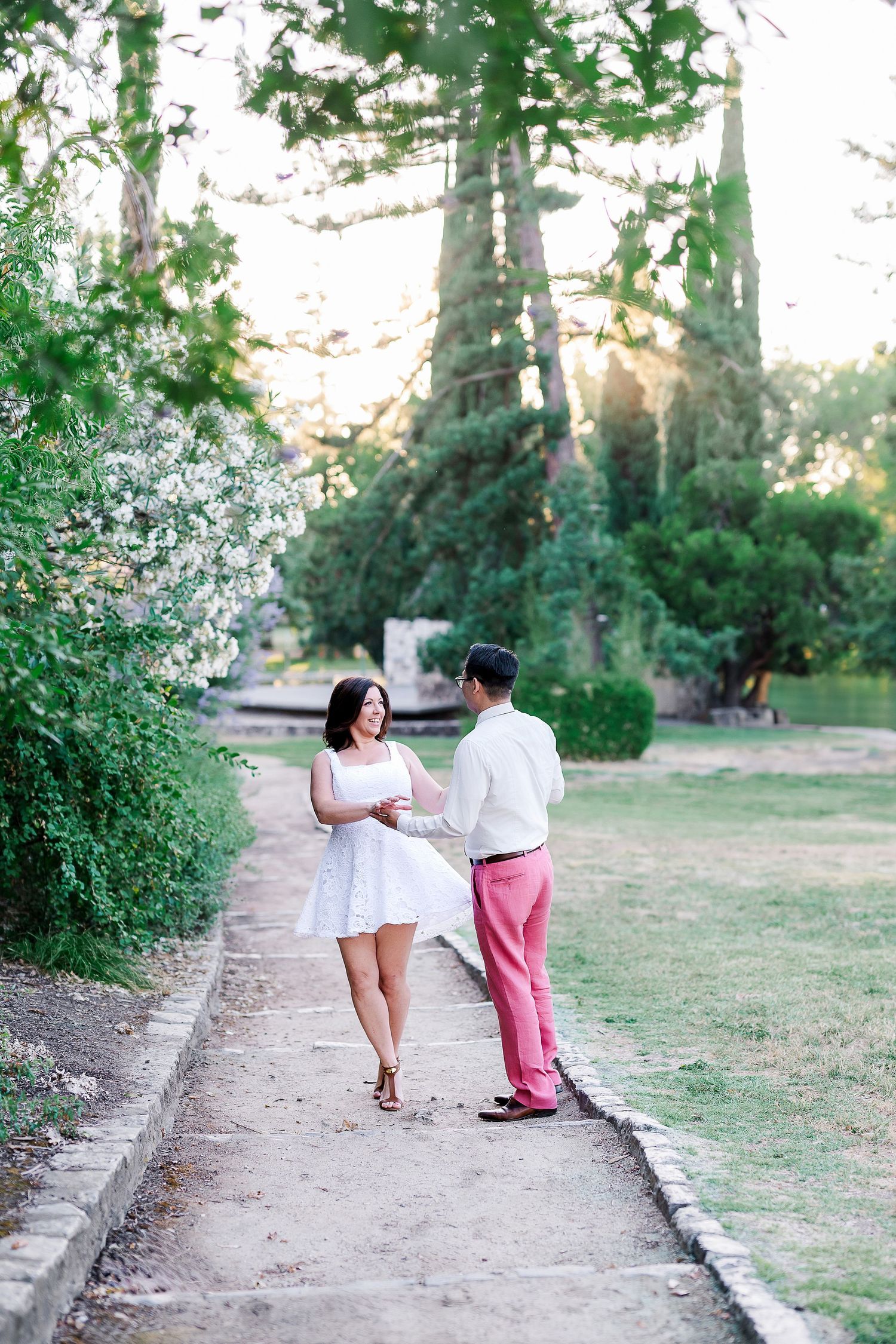 Couple walking together on a garden path surrounded by lush greenery and trees.