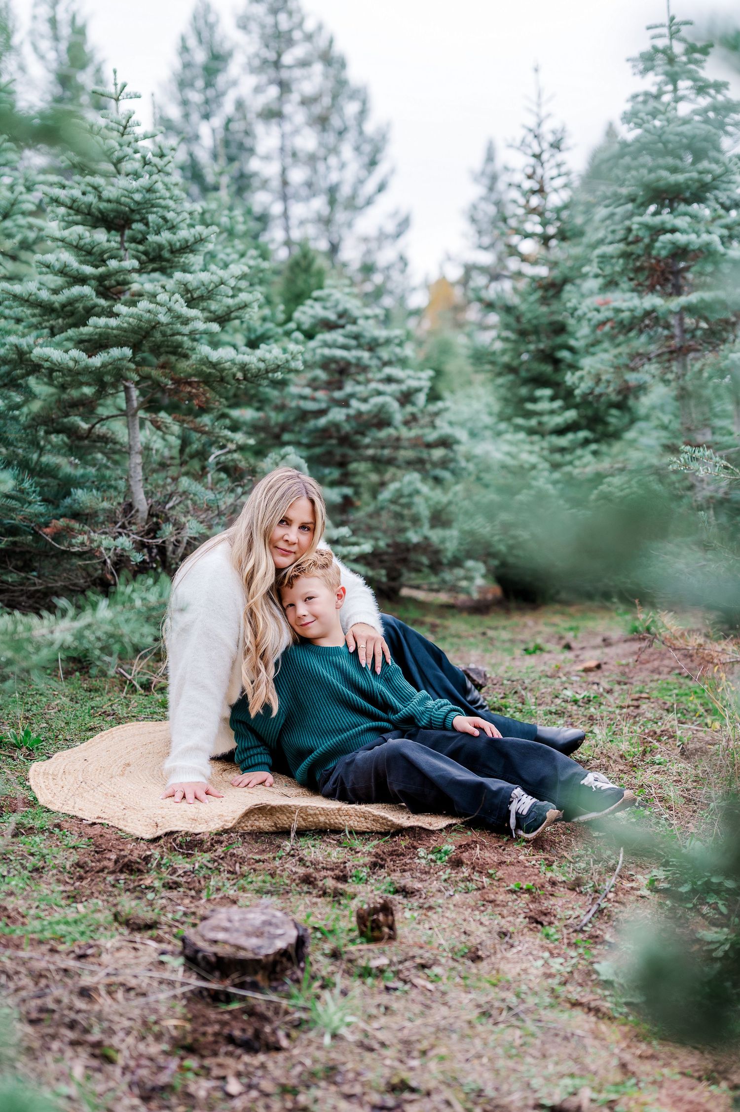 Couple laying together on forest floor surrounded by evergreen trees in romantic outdoor photo session.