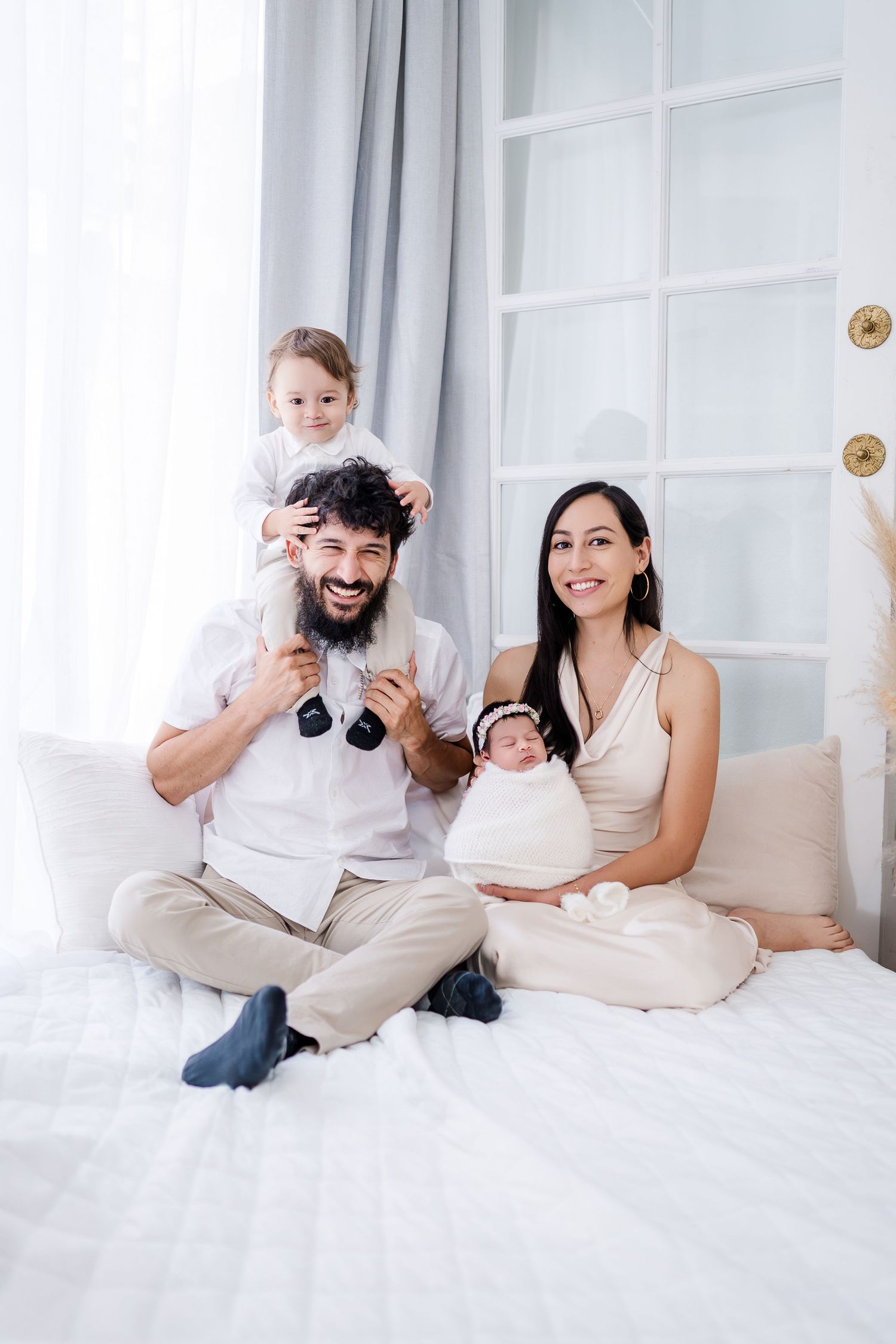 Family lounging together on white bedding while sharing joyful moments at home.