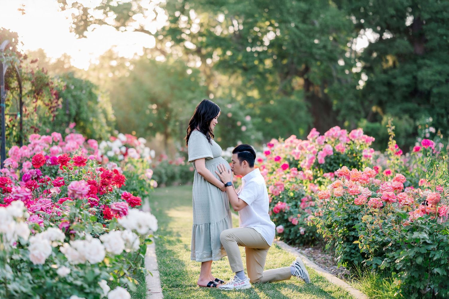 A couple embraces in a romantic garden setting filled with blooming pink roses during golden hour sunset.