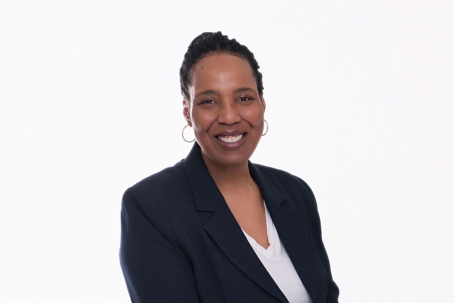Professional woman in black blazer smiling confidently against white background in corporate headshot photo.