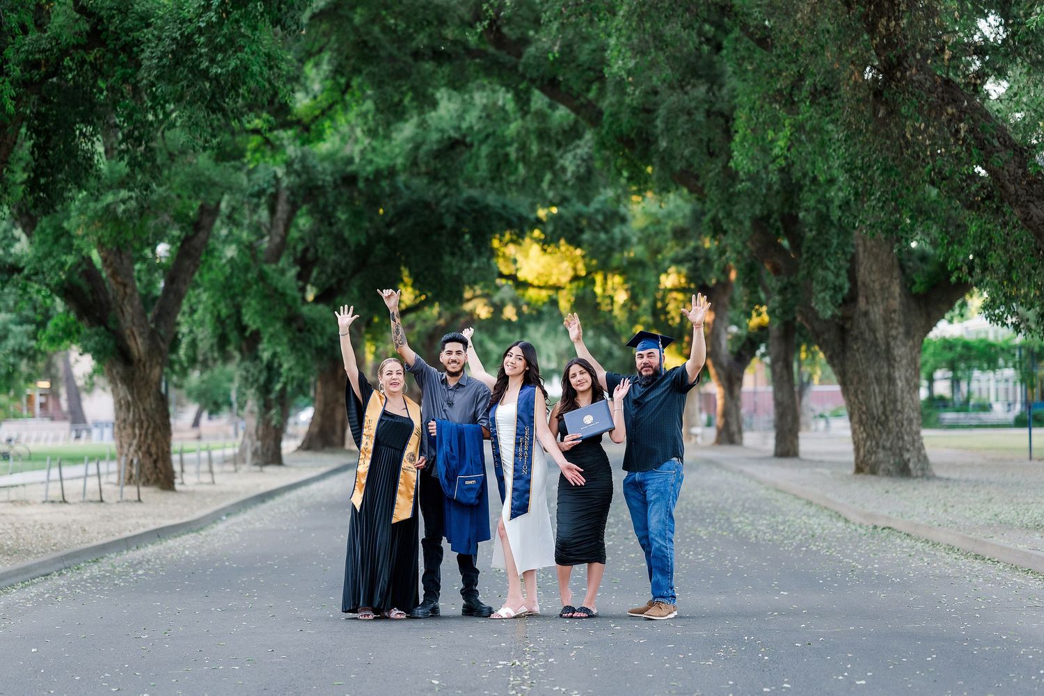 A group of people stand together on a tree-lined path in a park on a sunny day.