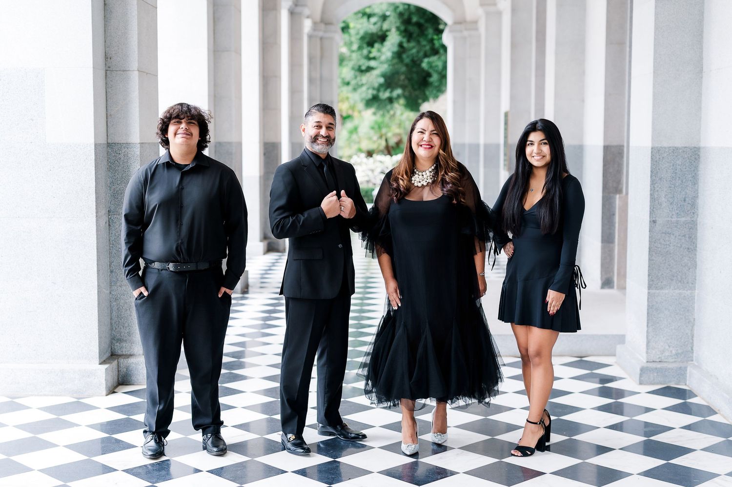 Dramatic family portrait session in black attire along elegant white colonnade walkway.