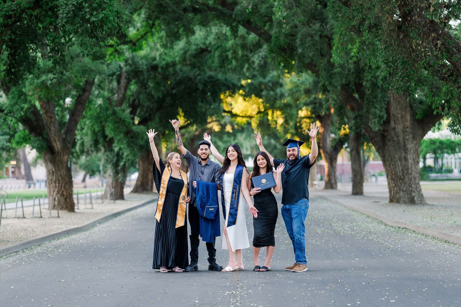 Group of people standing together on a tree-lined path at sunset.