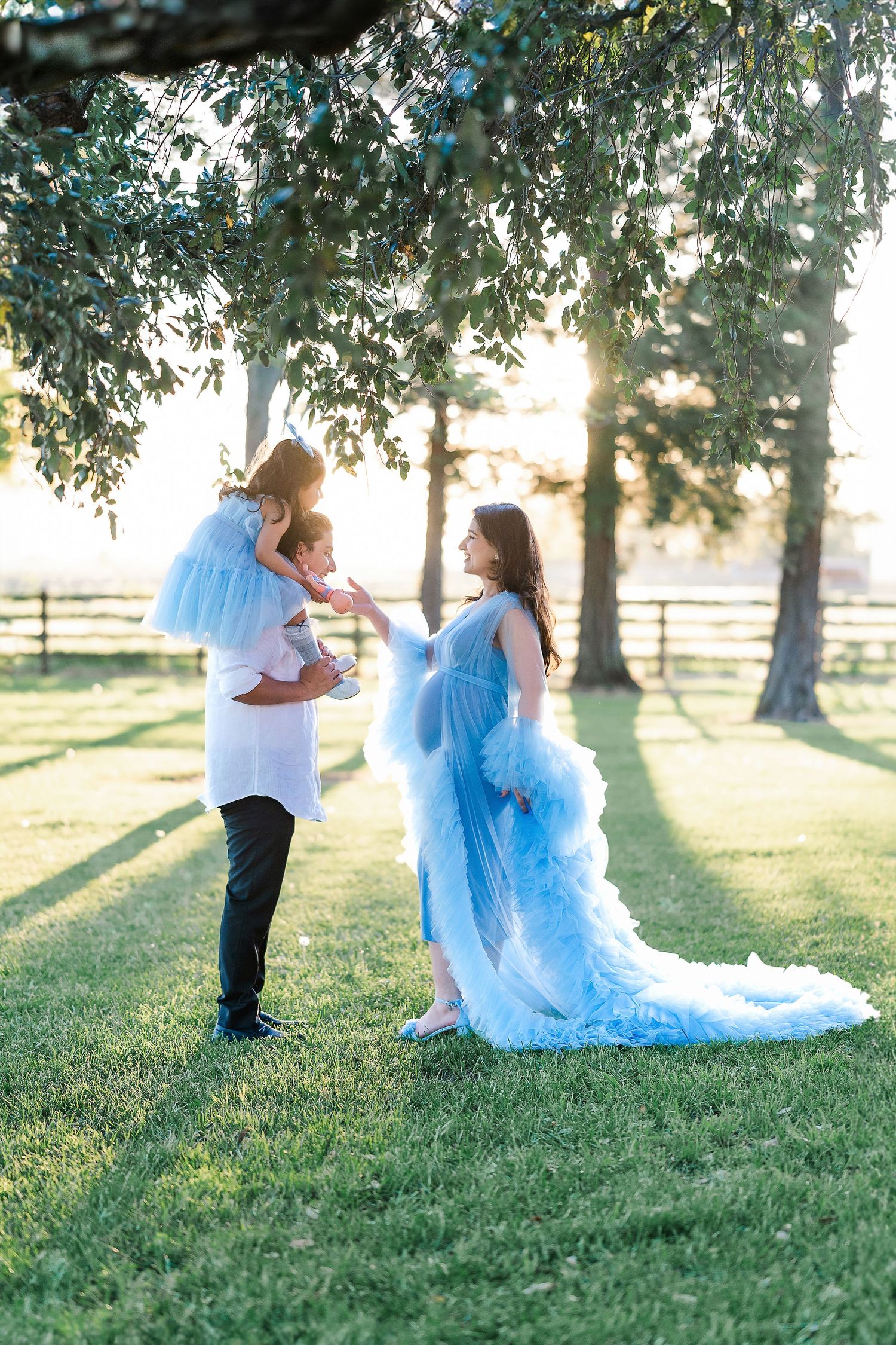 Family in matching blue tulle outfits posing in sunlit field with trees.