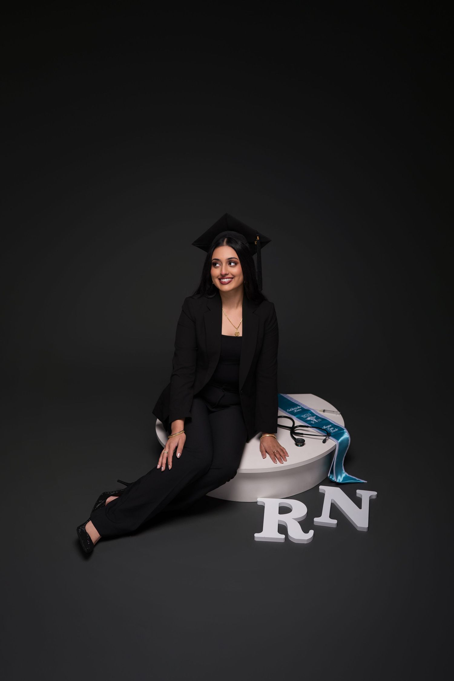 Professional portrait session showing someone in a black blazer posing with RN letters against dark background.