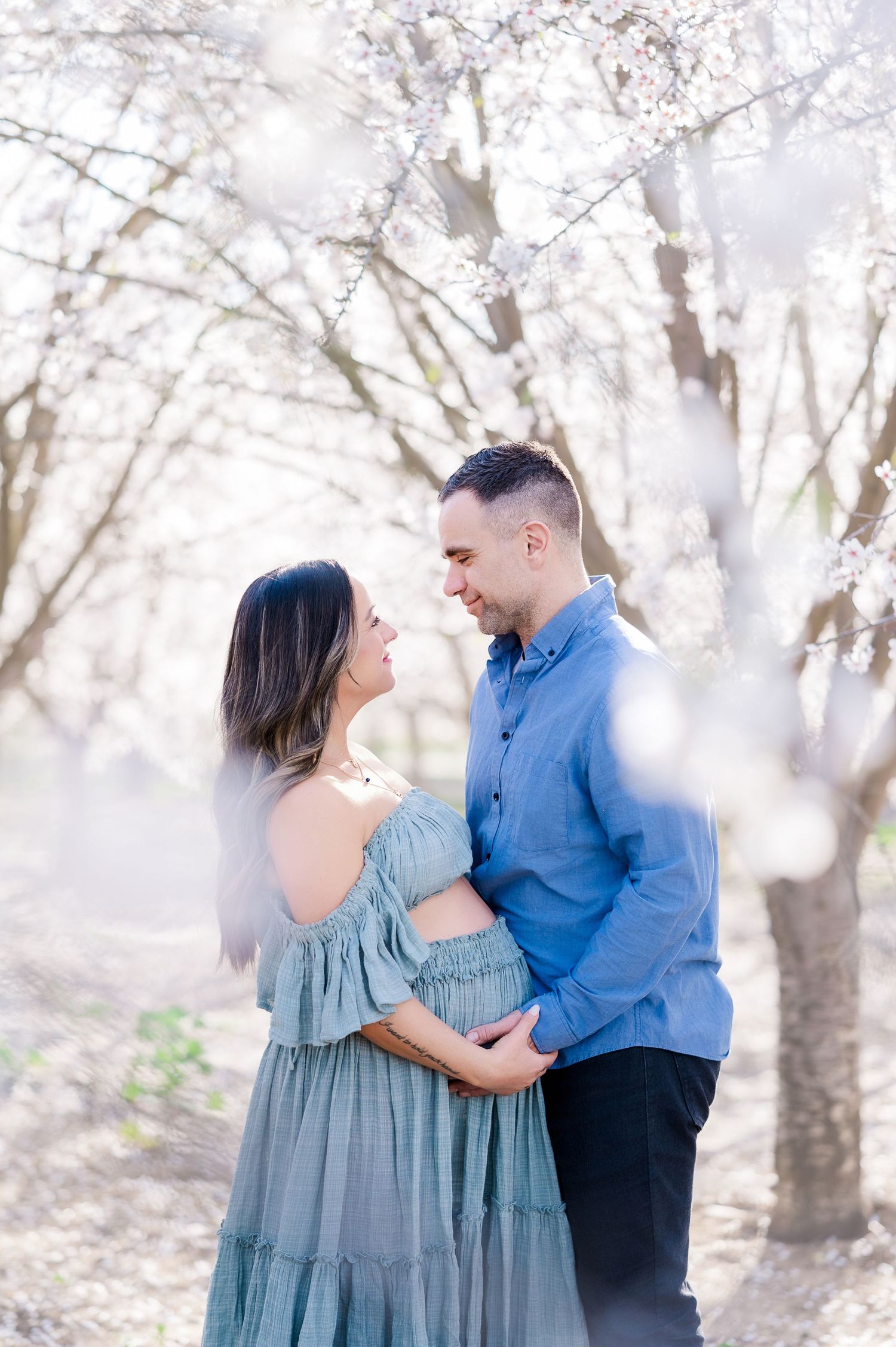 A couple shares tender moments in a dreamy outdoor setting wearing coordinated blue outfits.