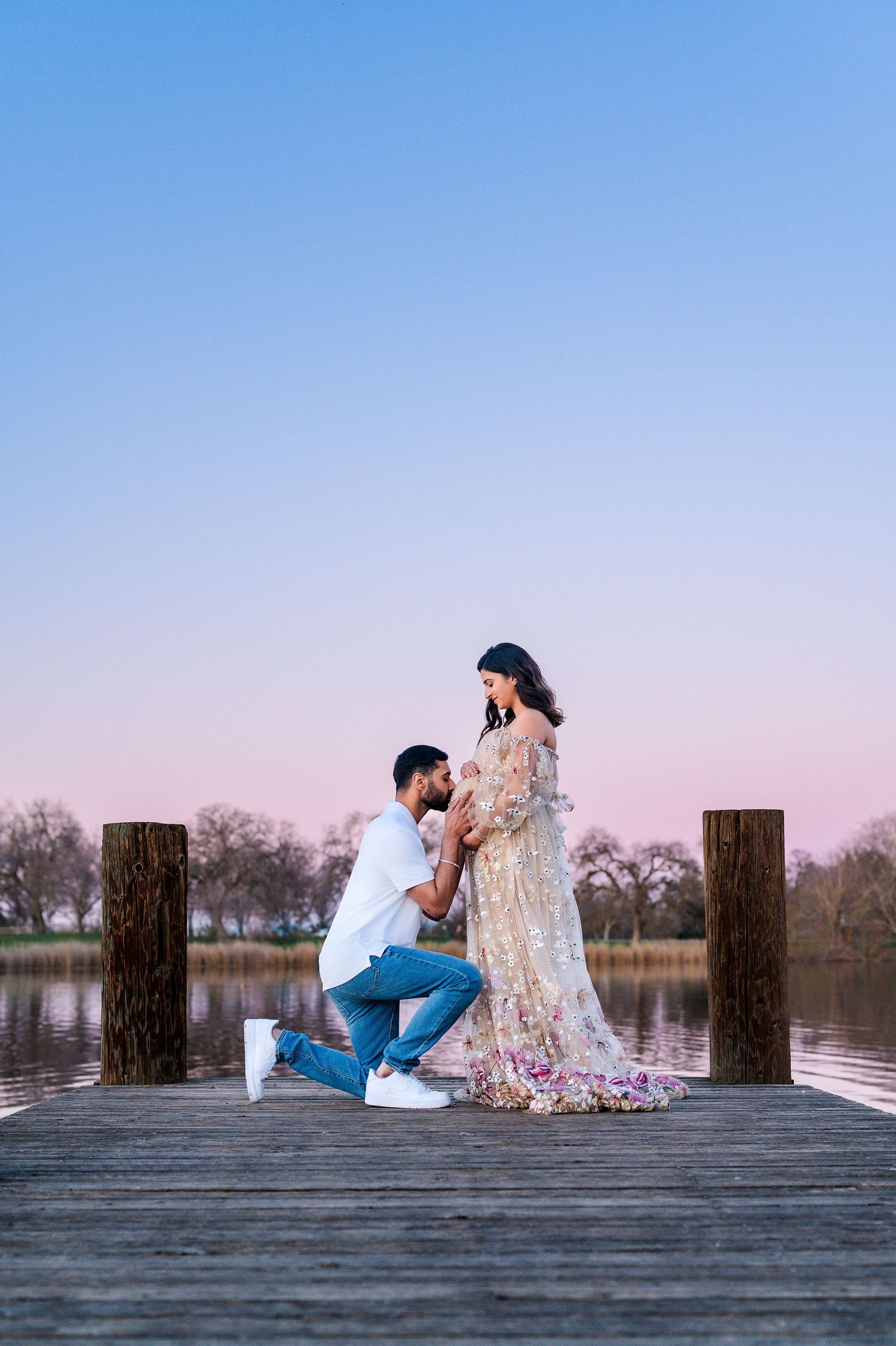 A couple sits together on a wooden dock by a serene lake during sunset creating a romantic silhouette.