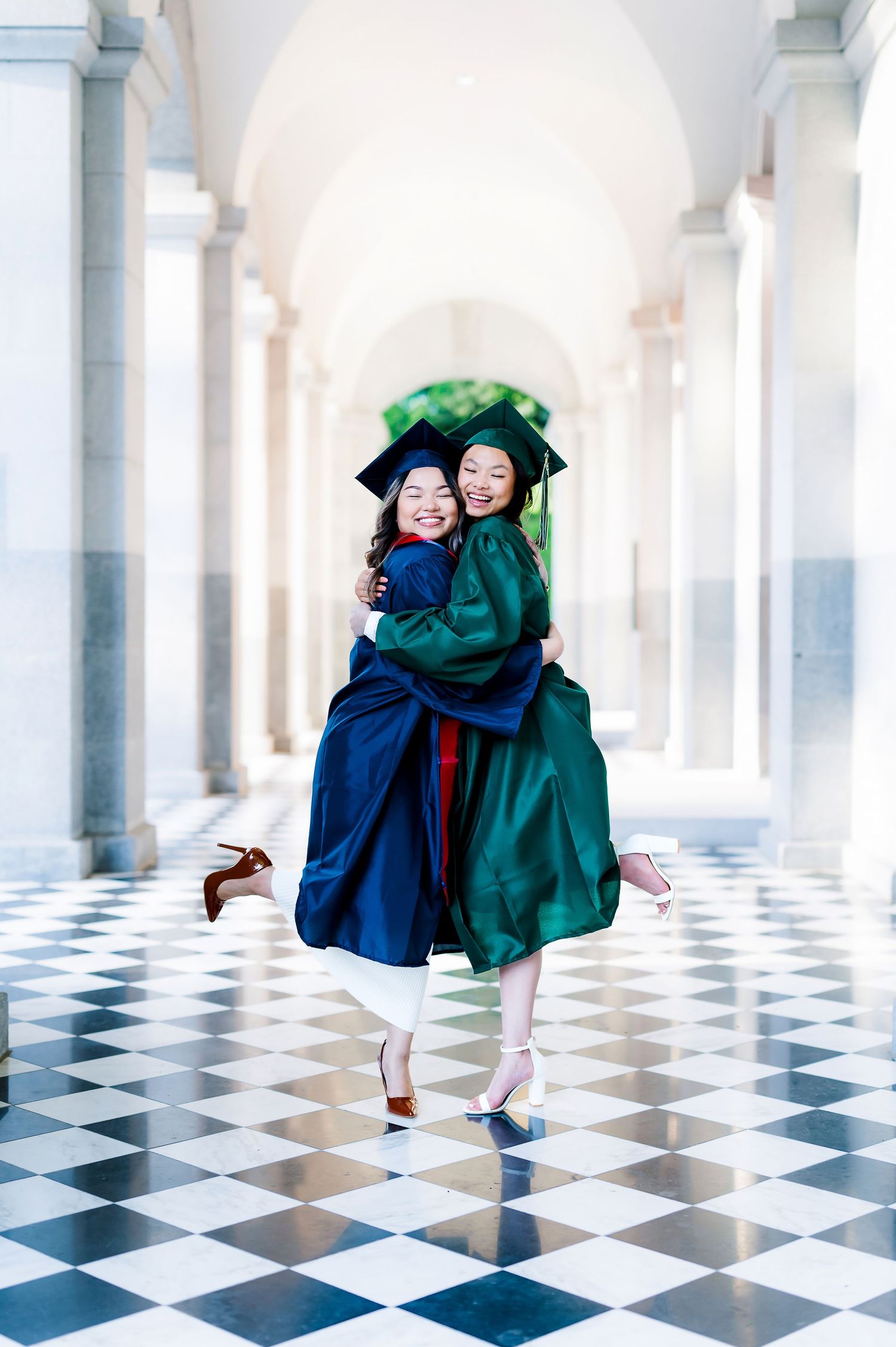 Graduates celebrate with joyful poses on checkered floor in elegant hallway.