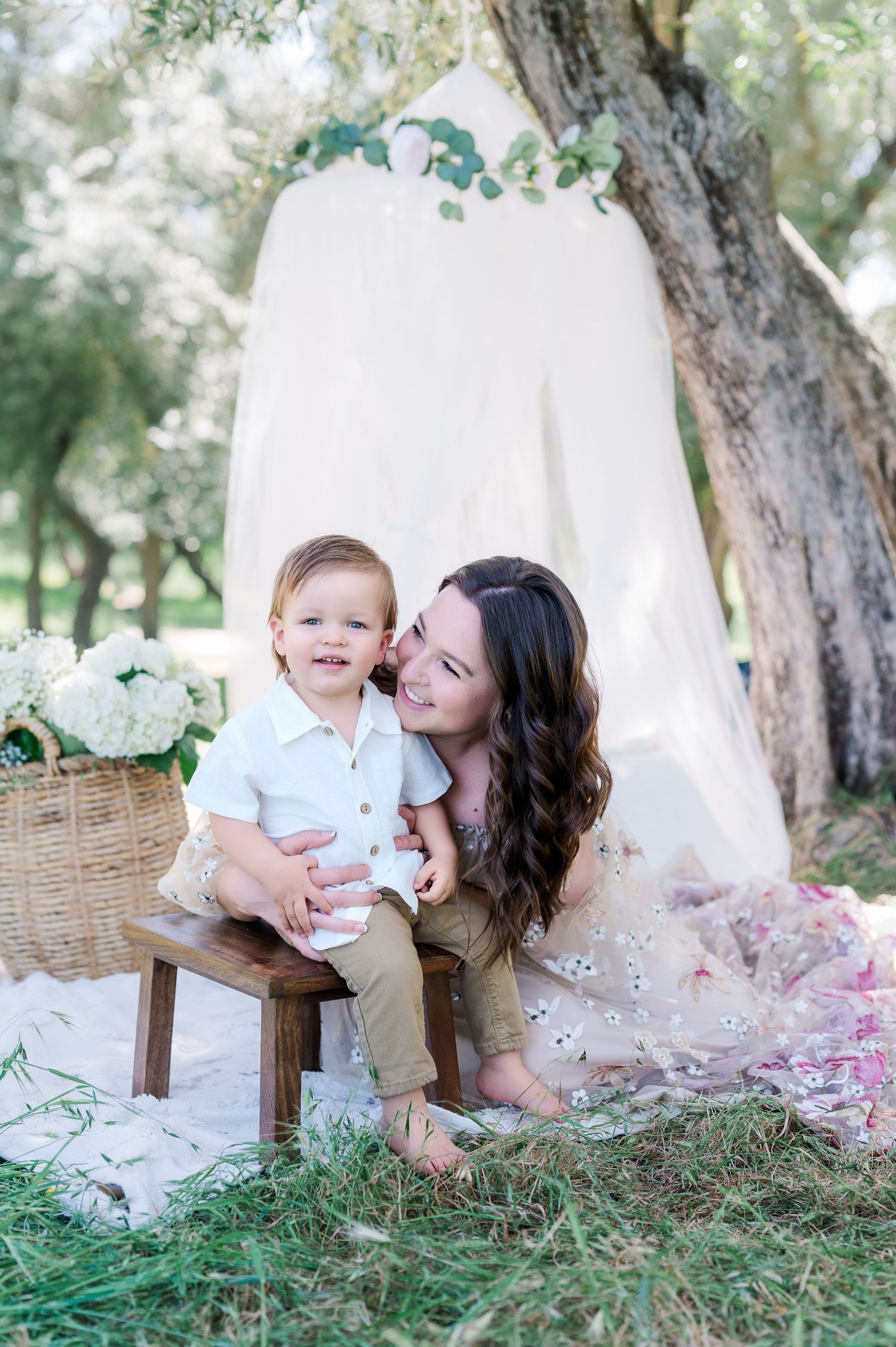 A dreamy outdoor portrait session with a white backdrop, floral decorations and a rustic wooden bench in a garden setting.