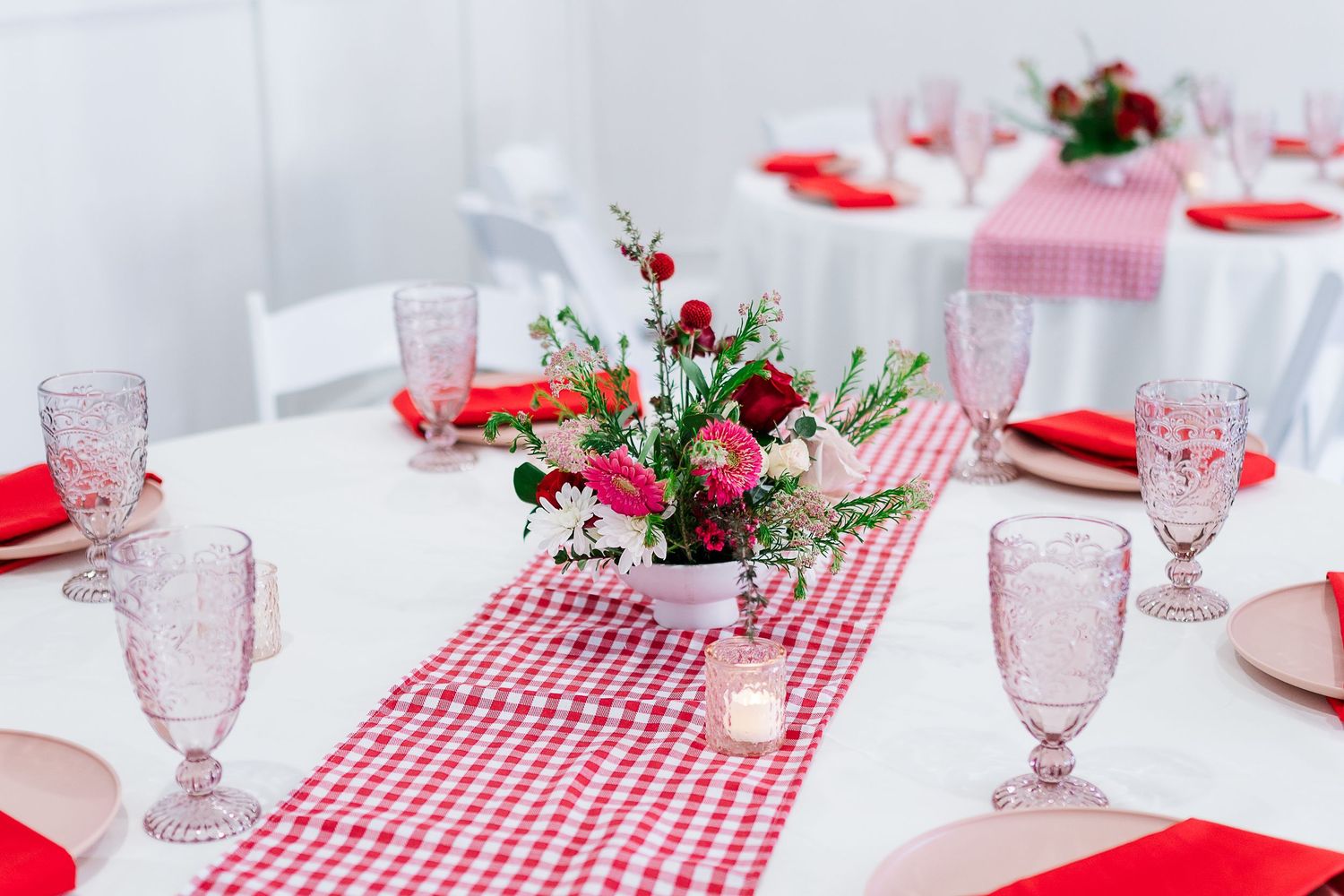 Elegant table setting with red gingham runner, pink glassware and fresh floral centerpieces.