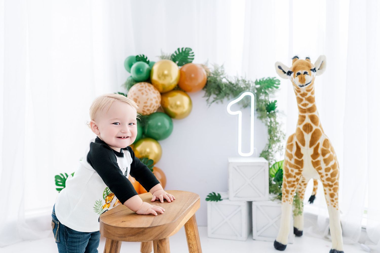 Baby's first birthday safari theme with giraffe toy, number 1, and jungle balloons in white studio.