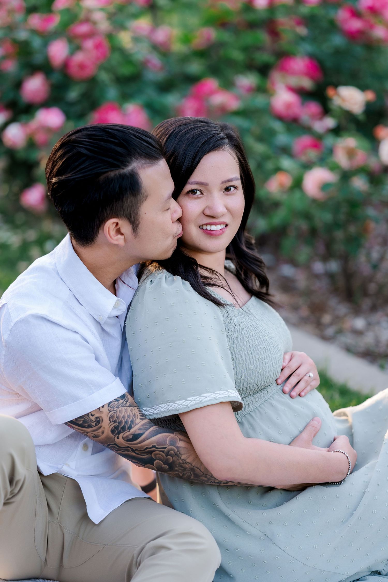 A tender maternity photo moment outdoors with pink roses in the background.