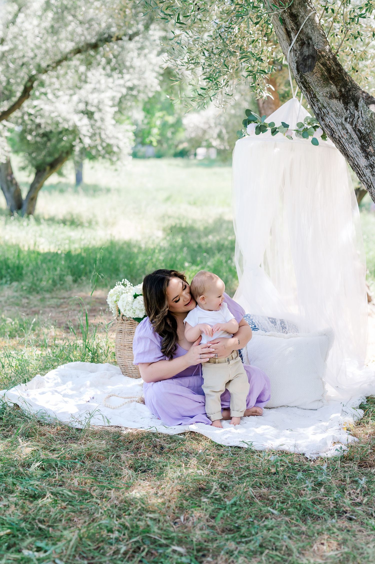 A tender moment shared on a white blanket under a tree in a peaceful outdoor setting.