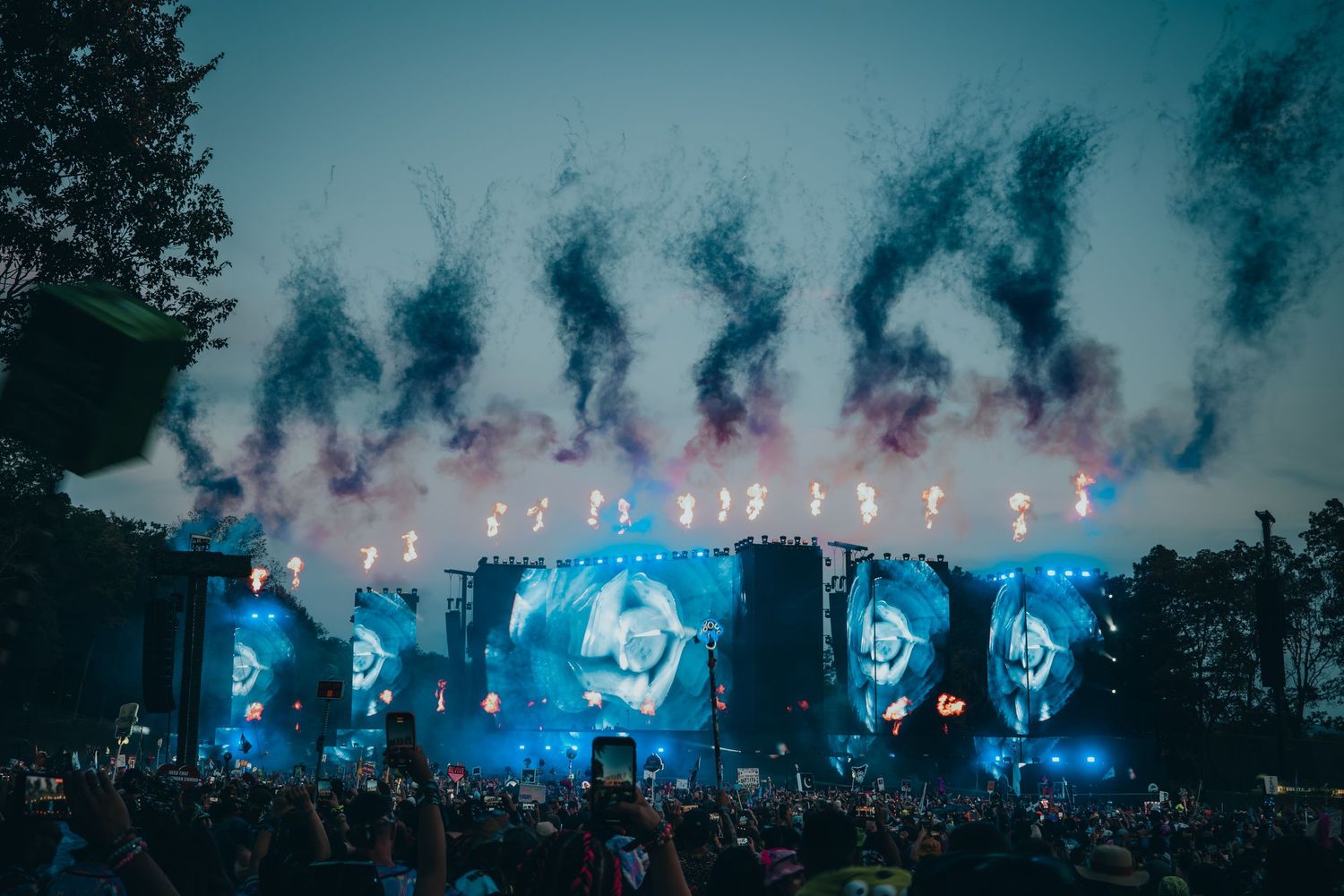 Concert stage illuminated with bright blue lights and smoke effects creates a dramatic atmosphere in an outdoor setting.