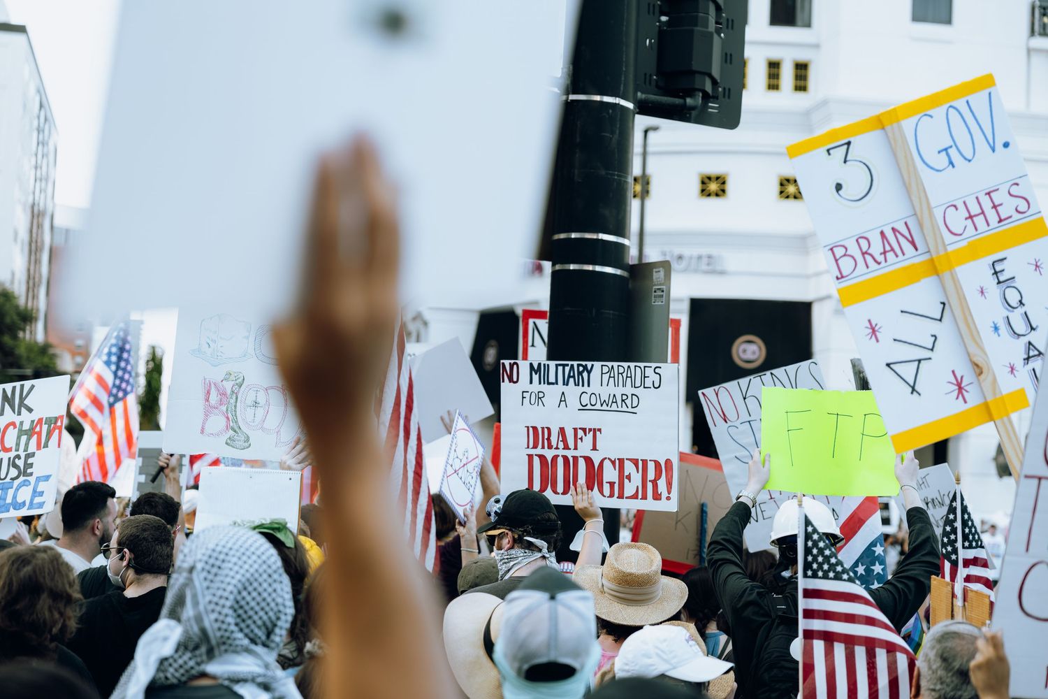 Crowd at protest gathering holds American flags and signs while raising hands during public demonstration.