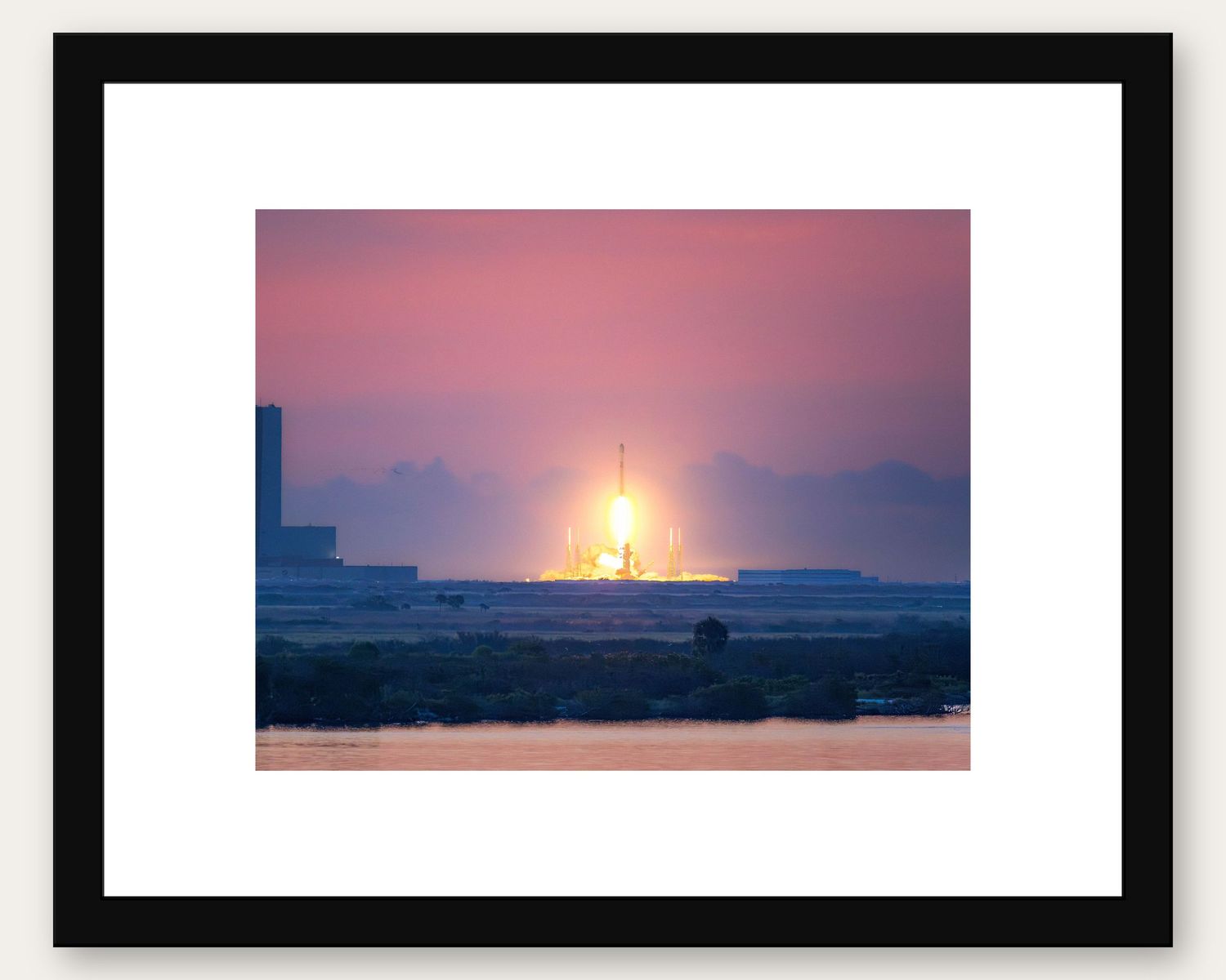 Framed photo of a rocket launch at sunset over a flat landscape, with vibrant pink and orange hues in the sky.