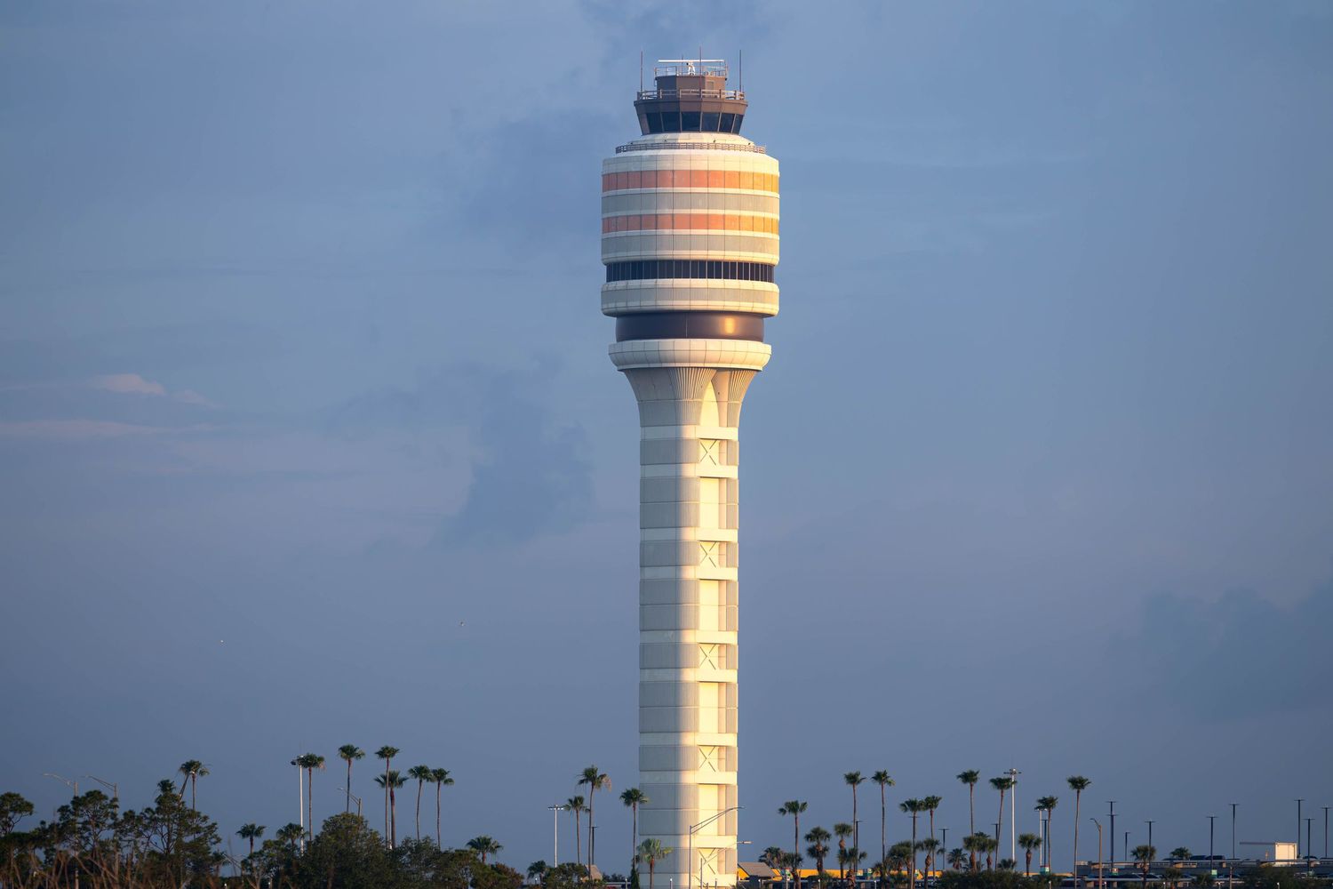 Illuminated air traffic control tower at Orlando International Airport against a dusk sky with palm trees.