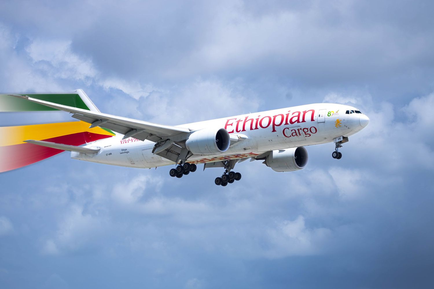 Ethiopian Cargo Boeing 777 freighter aircraft in flight against a cloudy blue sky, showcasing the airline's colorful tail livery.