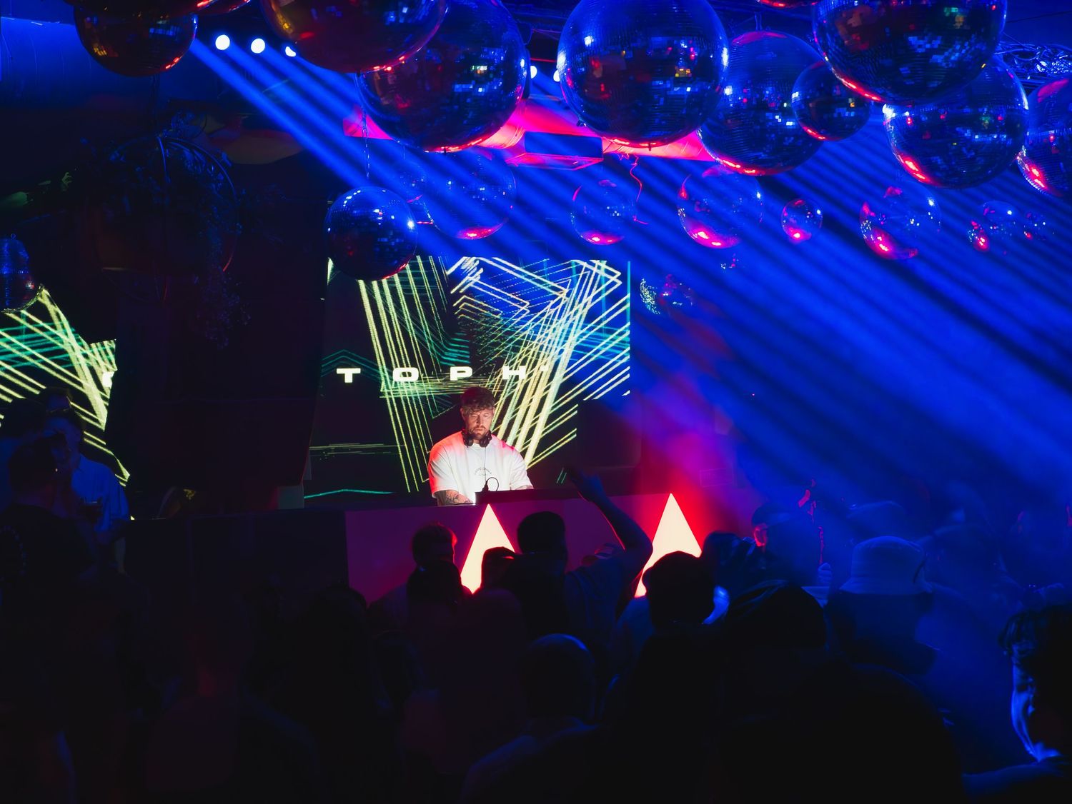 A nightclub scene with colorful laser lights in blue, red and green illuminating silhouettes of people dancing.