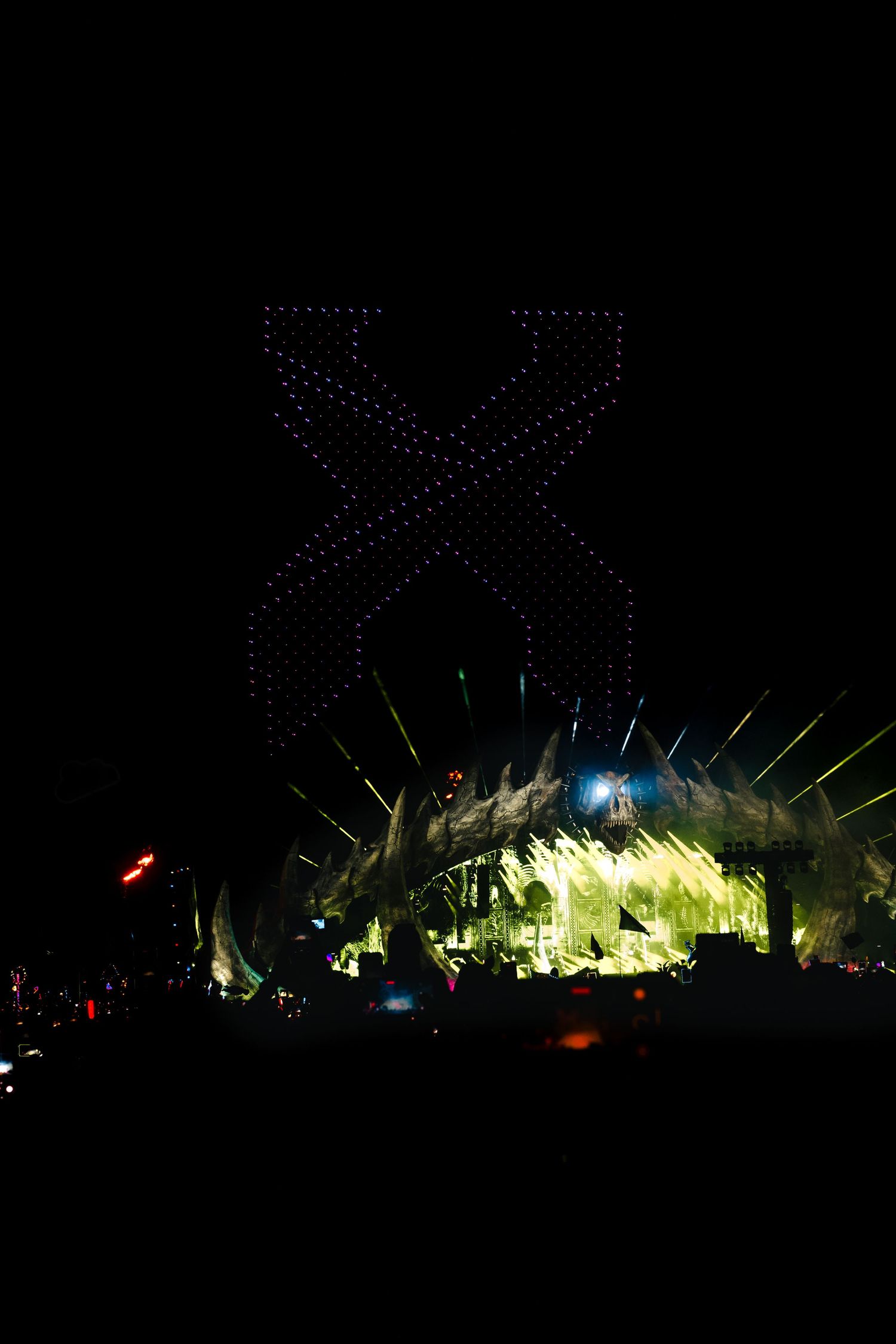Drone light show creates dazzling patterns against the dark night sky with illuminated structures visible below.