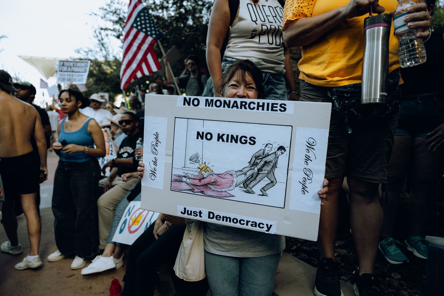 Protester holds 'No Monarchies No Kings Just Democracy' sign at street demonstration.