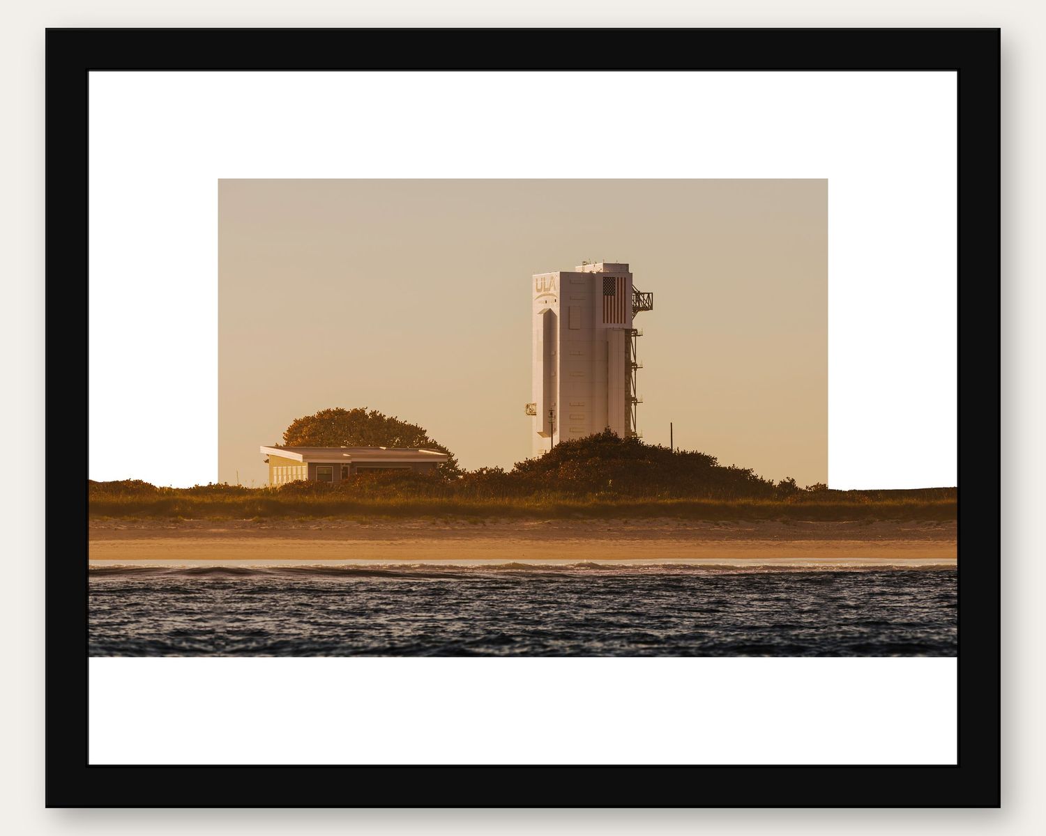 Framed photo of a rocket on a launch pad at golden hour, viewed from across calm ocean waters at Cape Canaveral.