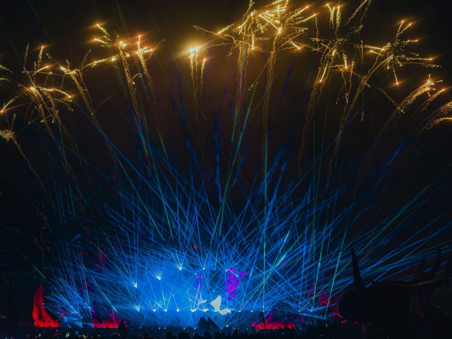 Colorful laser light show beams illuminate a dark venue with vibrant blue and red rays creating a dramatic atmosphere.