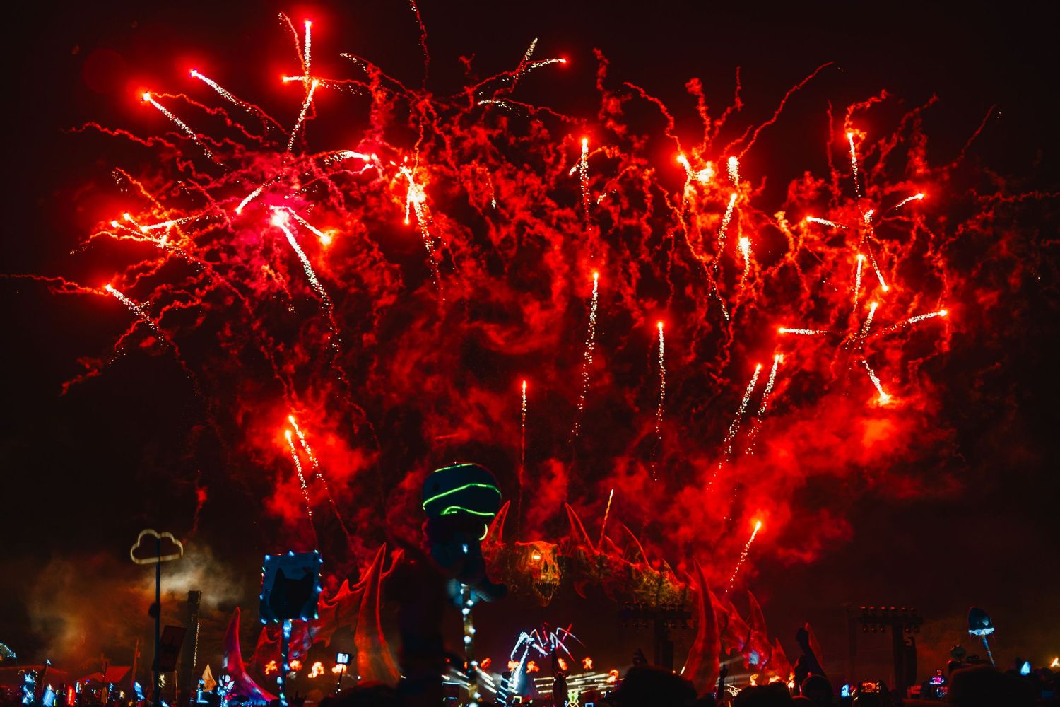 Red fireworks burst across the night sky in a spectacular display over a dark cityscape silhouette.