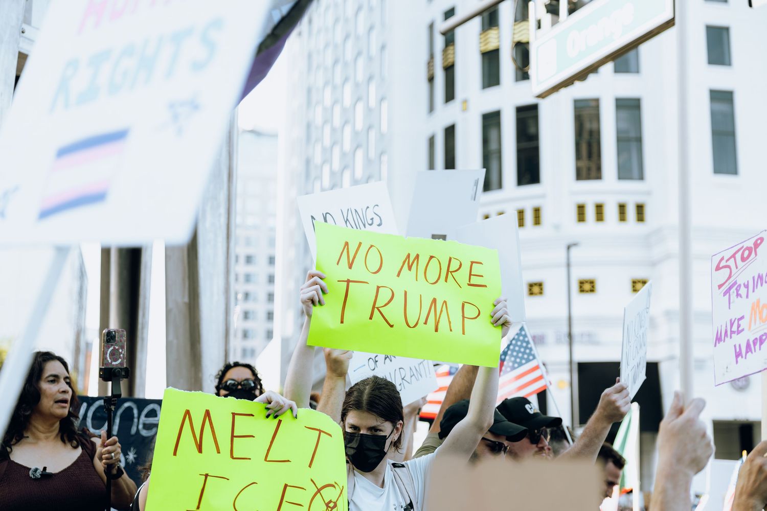 Protesters holding anti-Trump signs at outdoor political rally.
