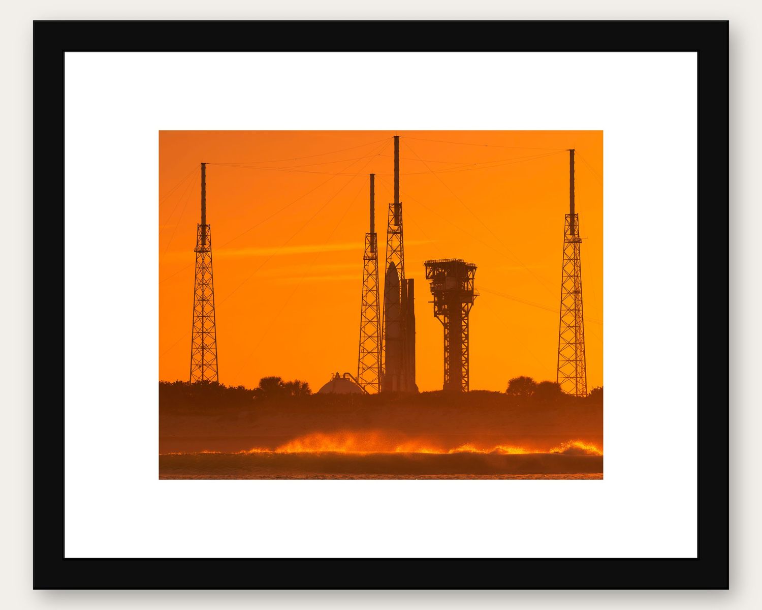 Framed photo of a rocket launch pad silhouetted against a vivid orange sunset sky at Kennedy Space Center.