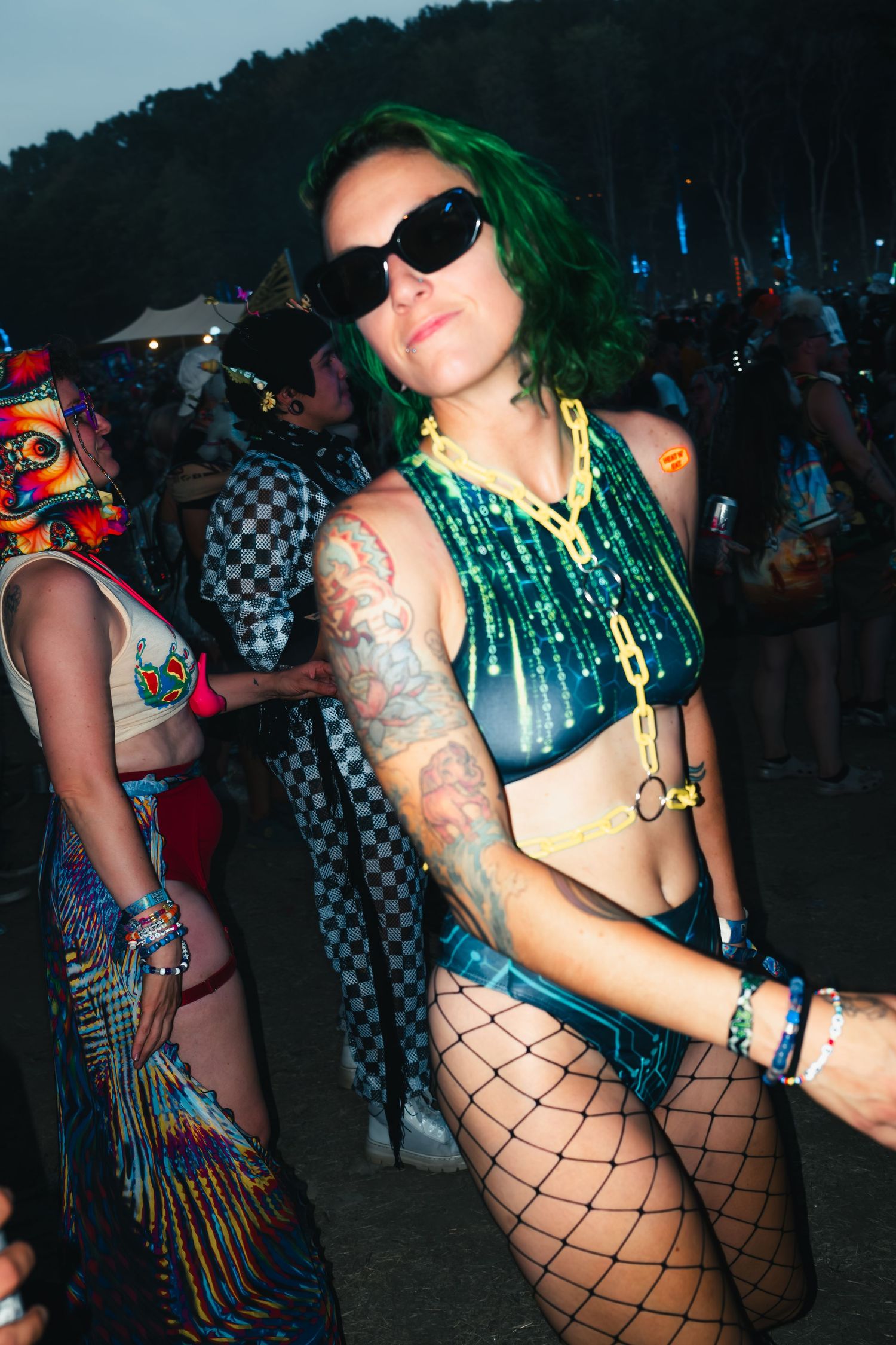 Dancers in festival attire with fishnet stockings and colorful outfits move energetically at a nighttime outdoor event.