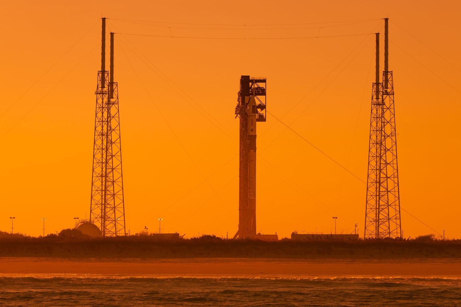 Rocket on launch pad silhouetted against vivid orange sunset sky at Cape Canaveral space center.