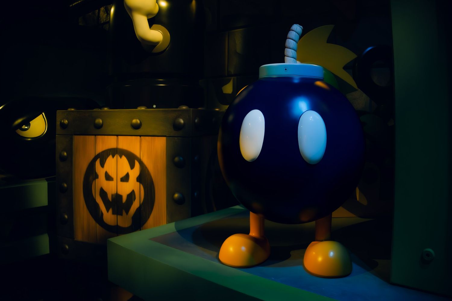 A spooky orange Halloween lantern stands next to a blue cartoon bomb decoration with white eyes and yellow feet in dark lighting.