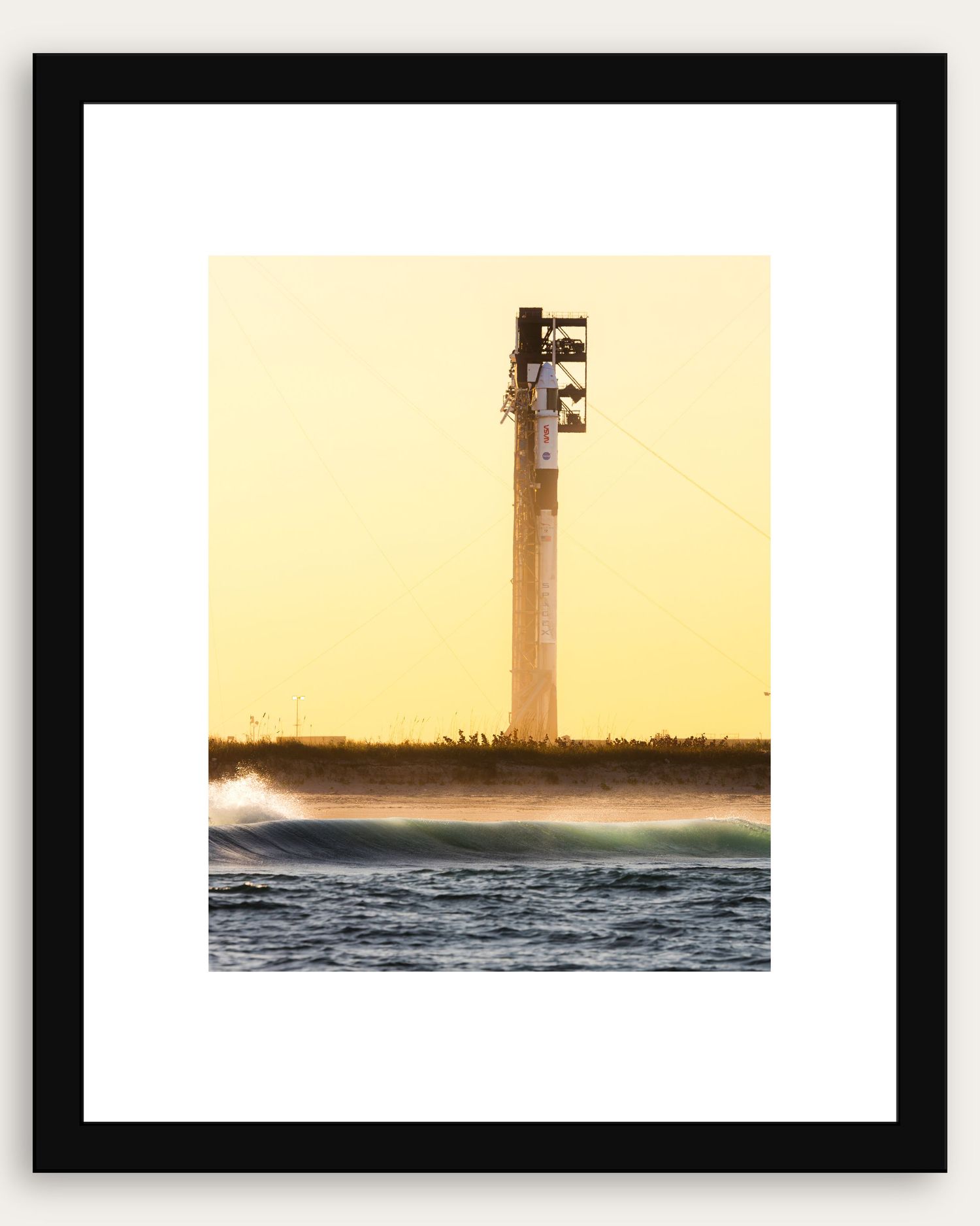 Framed photo of a tall tower at golden sunset with ocean waves in the foreground, coastal landscape art print.