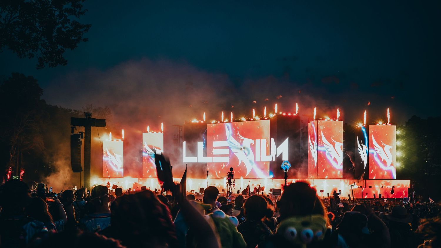 Concert stage illuminated with vibrant red lights and smoke effects during an outdoor nighttime performance.