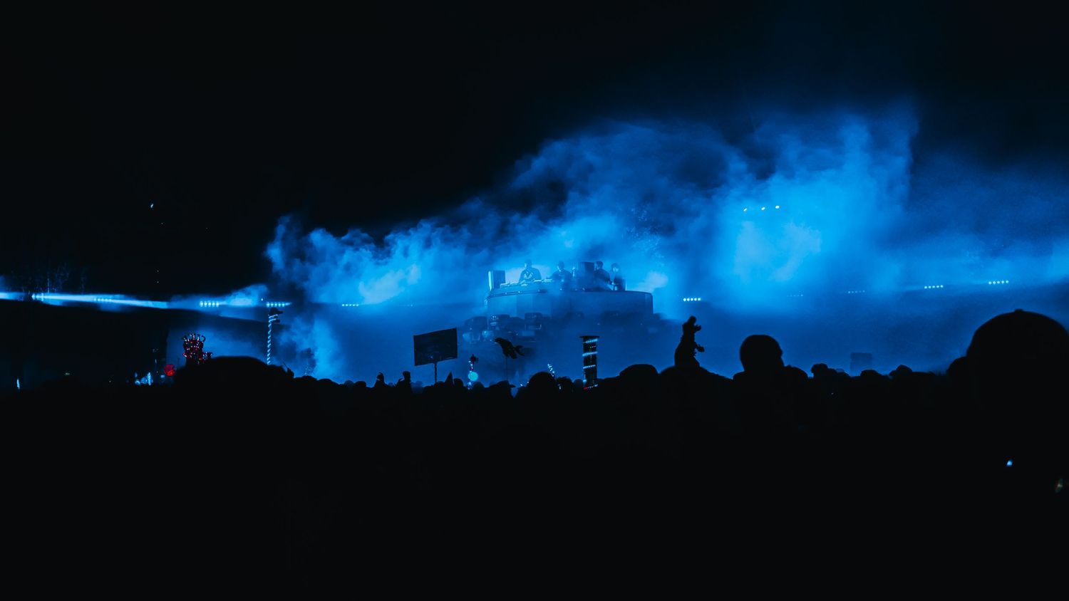 A dramatic panoramic view of a dark stormy sky with glowing blue clouds illuminated against a black horizon.