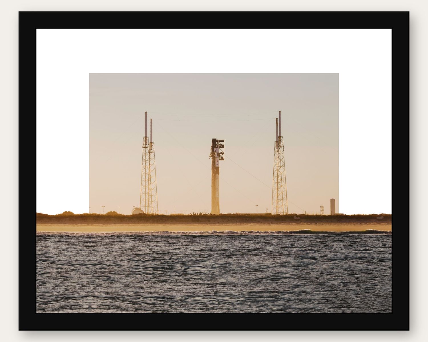 Framed photo of a rocket on a launch pad at sunset with water in the foreground at Kennedy Space Center.