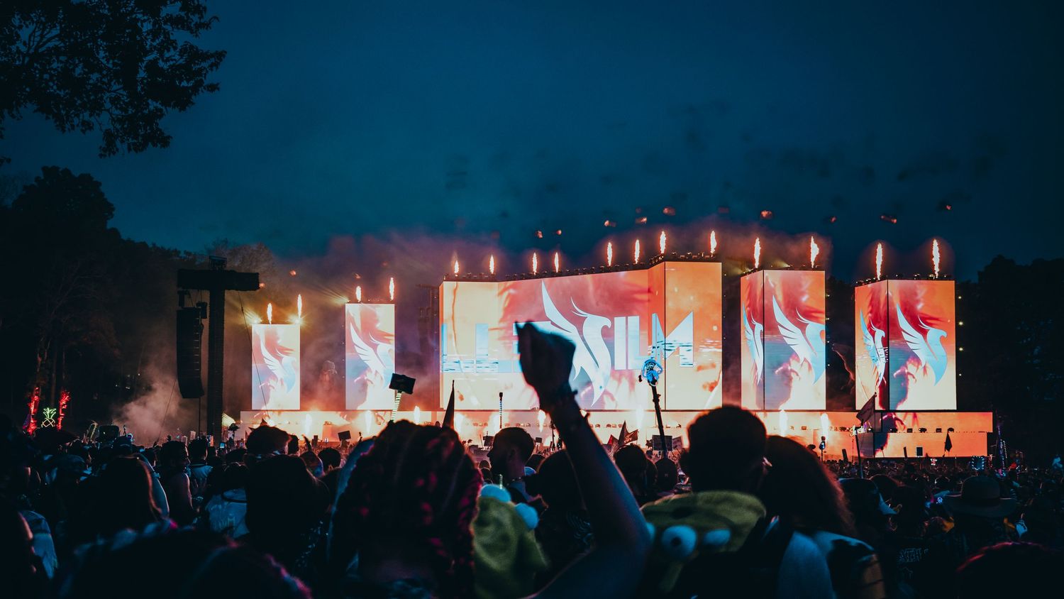 A panoramic view of an outdoor concert venue at night with illuminated stages and crowd silhouettes.