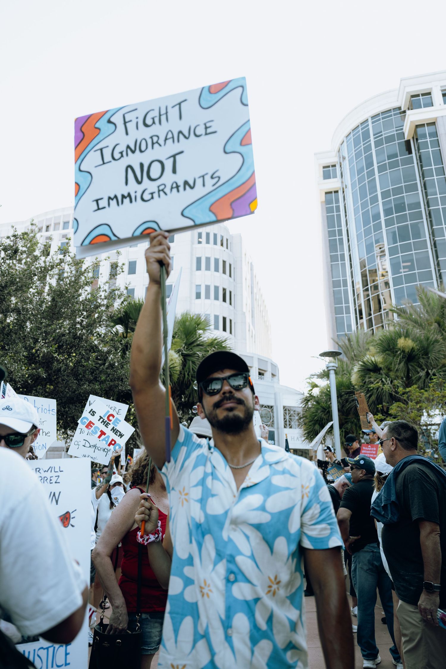 Demonstrator holding protest sign reading 'Fight Ignorance Not Immigrants' in urban setting.