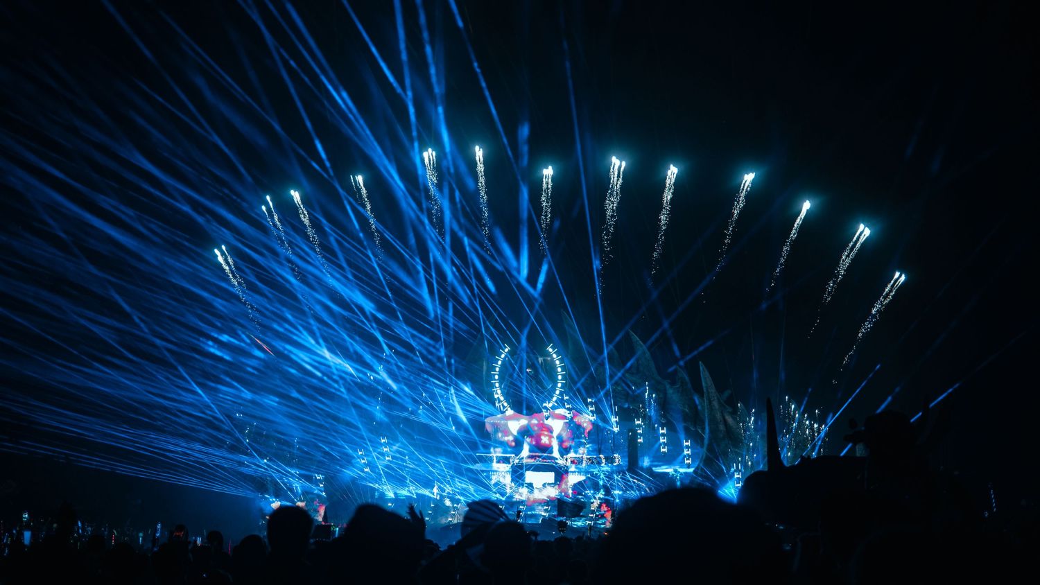 Blue laser beams illuminate a dark concert stage during a live performance at night.