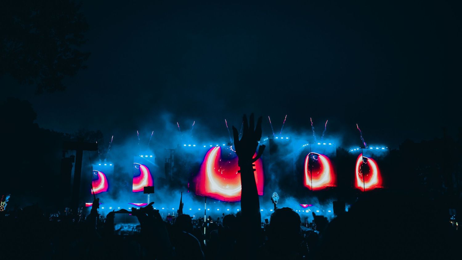 Silhouettes of concert crowd illuminated by vibrant blue stage lights during a nighttime performance.