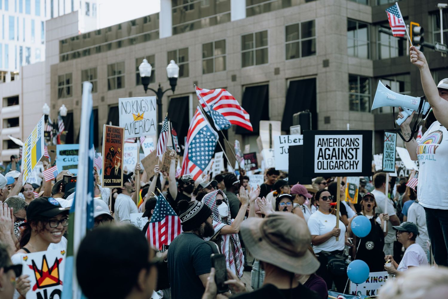 A large crowd of protesters wave American flags and signs in an urban setting.