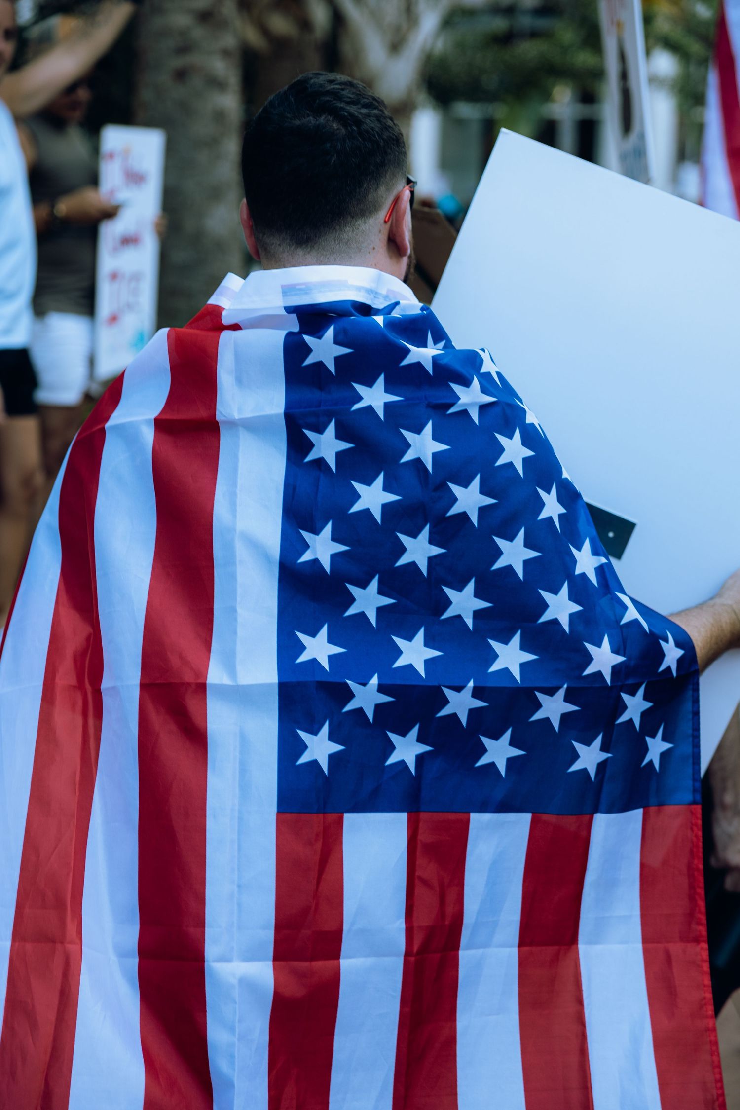 Person draped in American flag at protest with city buildings in background.
