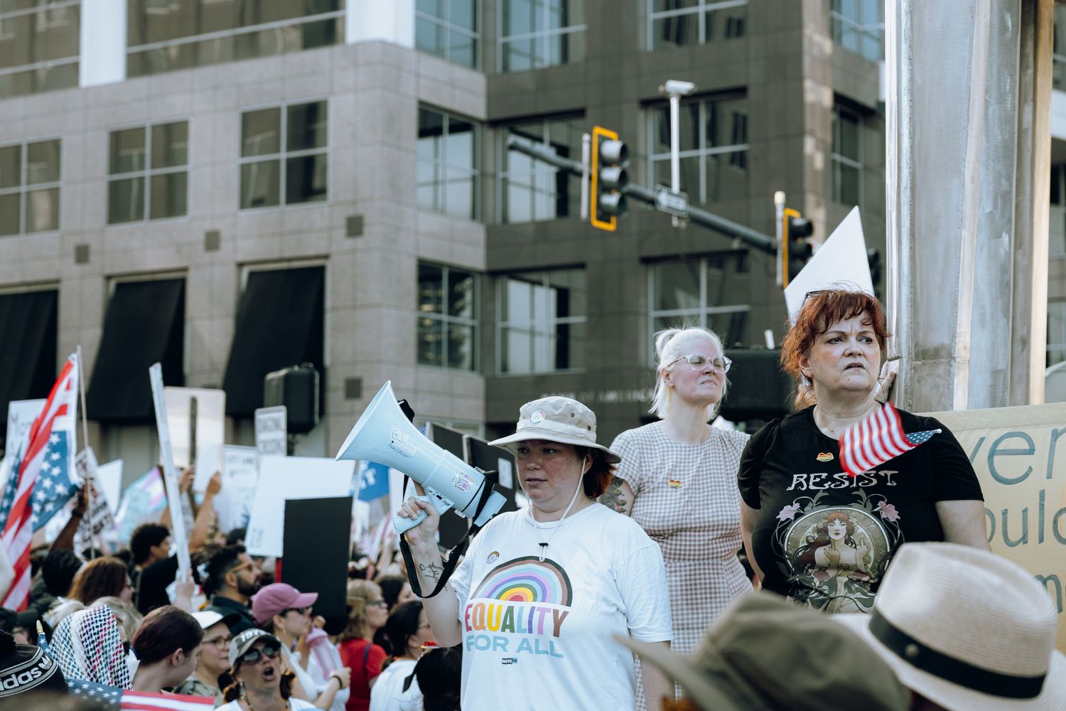 A crowd of protesters gather on a city street corner carrying flags and signs during a demonstration.