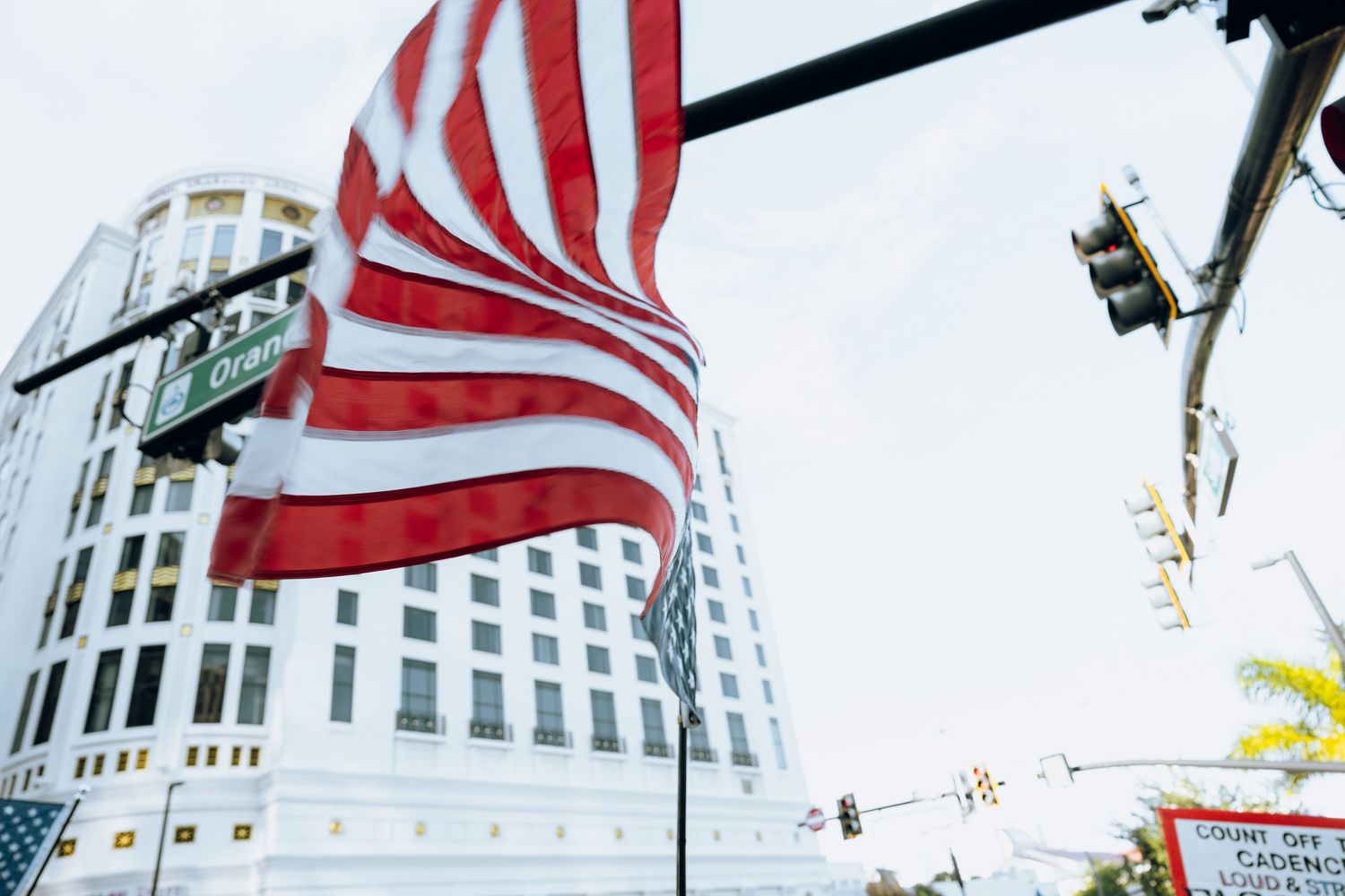 American flag waves against modern urban skyline with traffic lights visible.
