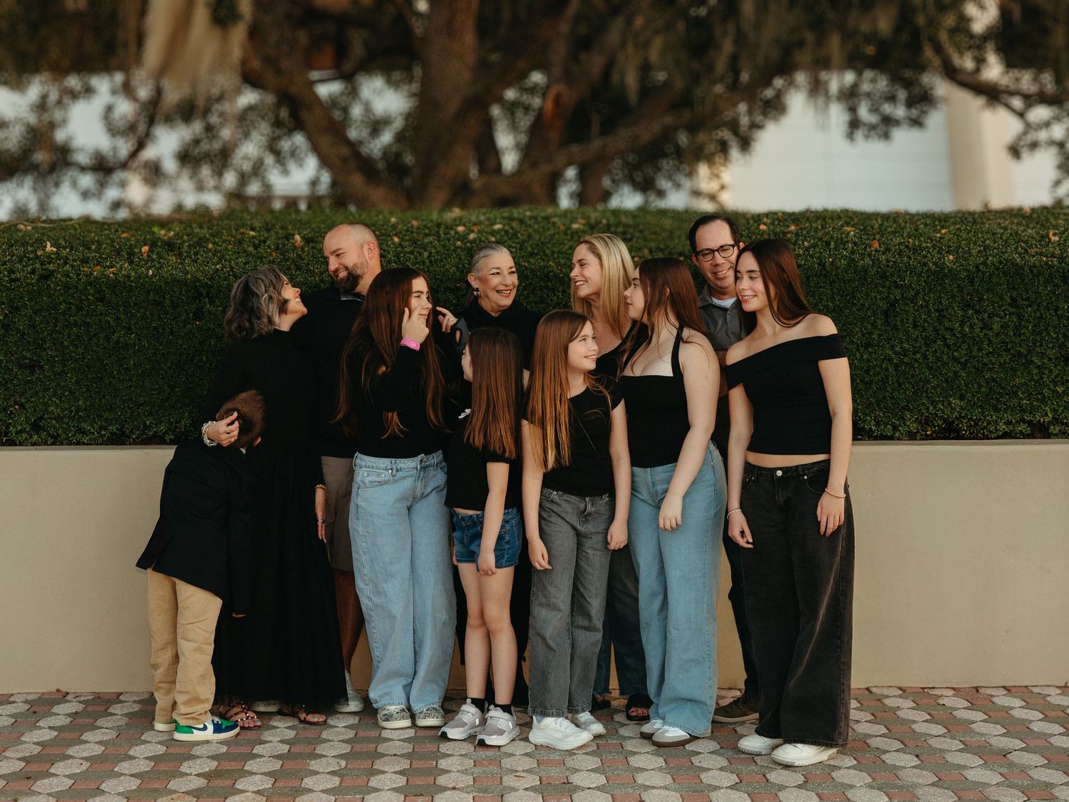 A group of people in casual attire pose together against a green hedge wall during golden hour.