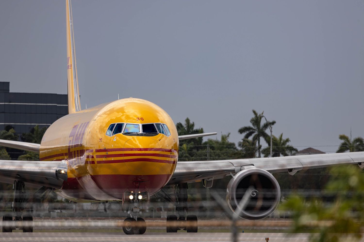 DHL cargo Boeing 757 aircraft taxiing on runway, yellow livery, tropical airport setting.